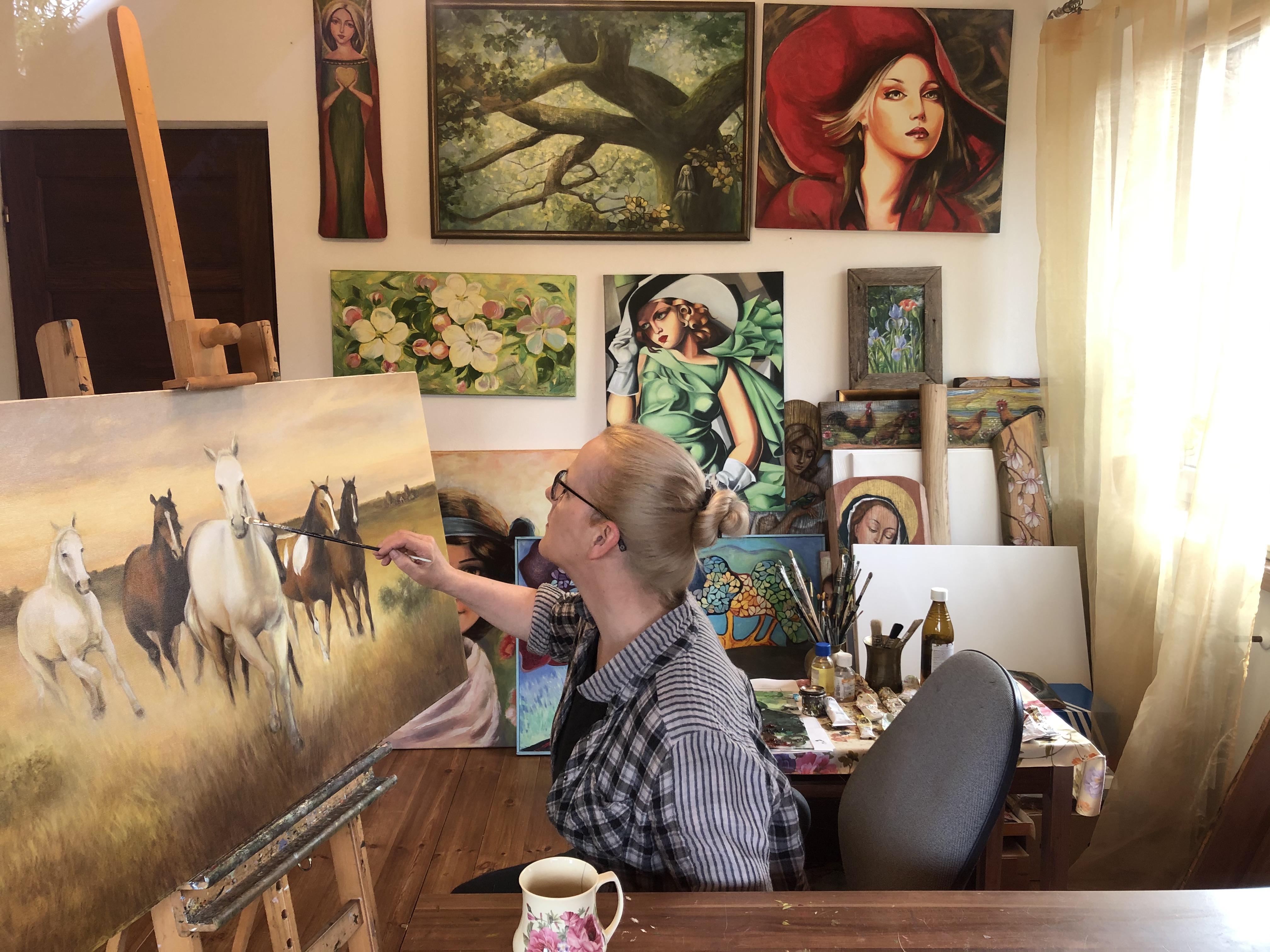 Ilustracja 1: Malarka w swojej pracowni maluje obraz stado koni.